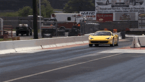 a yellow sports car is driving down a race track in front of a billboard that says repair and service