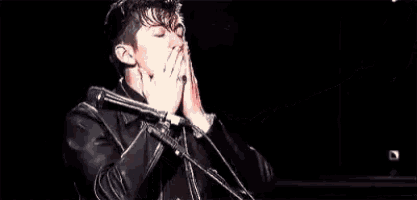a young man in a leather jacket is standing in front of a microphone .