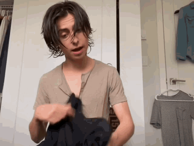a young man in a tan t-shirt is holding a black shirt