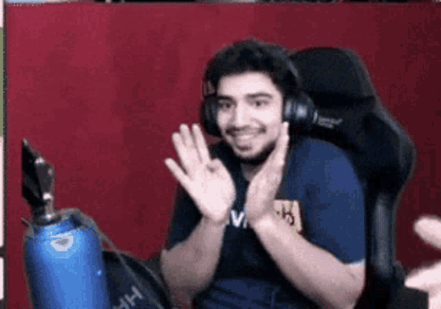 a man wearing headphones and a blue shirt is sitting in a chair and waving .