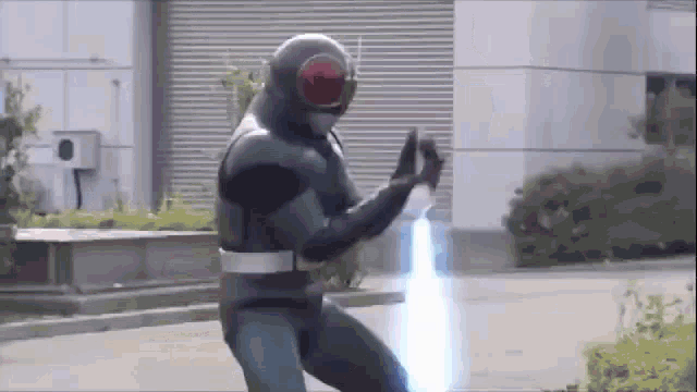 a man in a superhero costume is standing in front of a building with a light coming out of his hands .