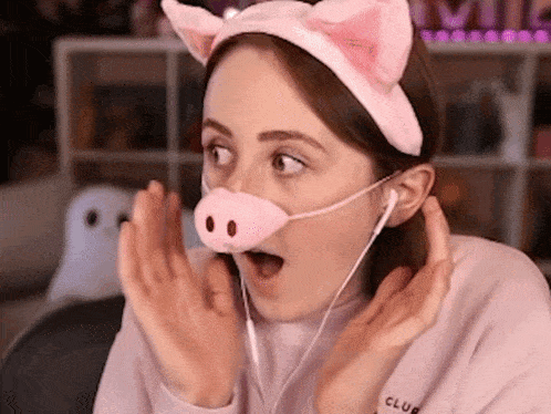 a woman wearing a pig headband and ear buds has a pig nose on her face .