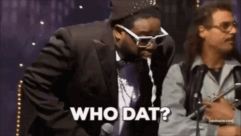 a man in a suit is talking into a microphone while another man stands behind him and says who dat .
