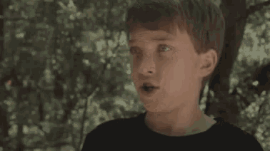 a young boy is standing in the woods with his mouth open and looking up .