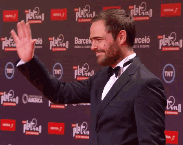 a man in a tuxedo is waving his hand in front of a wall that says tnt