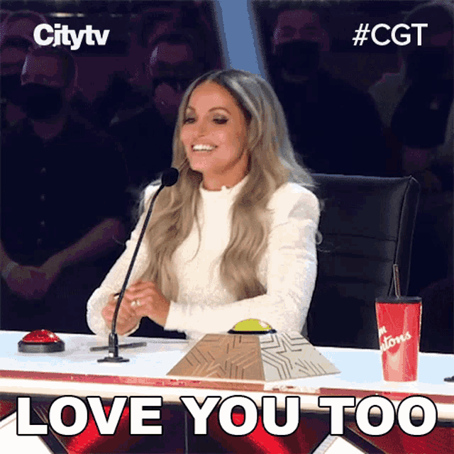 a woman sitting in front of a microphone with the words love you too written on the bottom