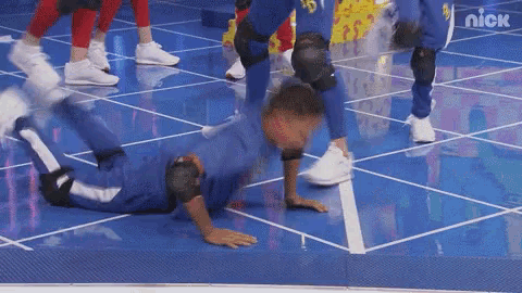 a man is doing a handstand on a blue tiled floor while a group of people are standing behind him .