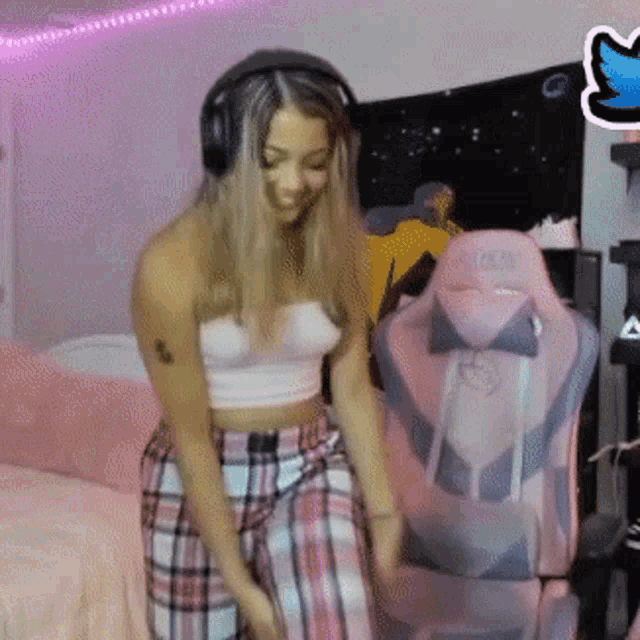 a woman wearing headphones and plaid pants is dancing in front of a gaming chair