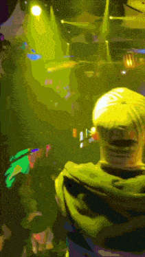 a man in a green hoodie is standing in front of a stage with a yellow light shining on him