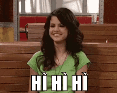 a woman in a green shirt is smiling and sitting in a booth with a sign that says hi hi hi .
