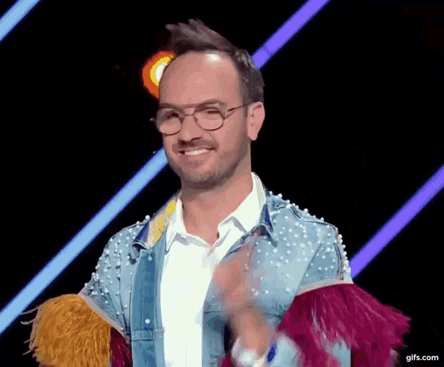 a man wearing glasses and a denim jacket with feathers on the sleeves is clapping