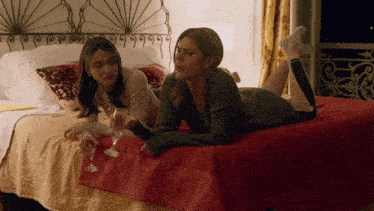 two women laying on a bed drinking wine