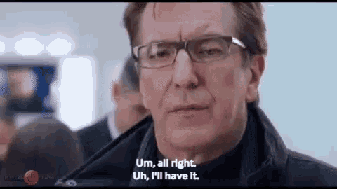 a man wearing glasses and a black jacket is talking to another man in a crowd .