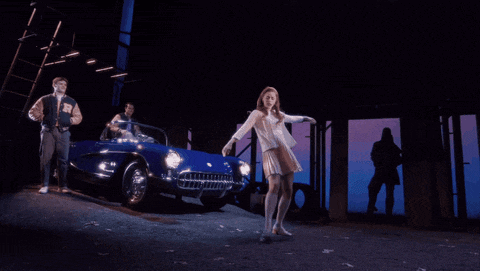 a man in a varsity jacket is driving a blue car