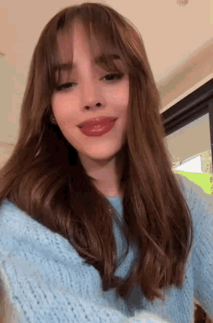 a woman with long brown hair is wearing a blue sweater .