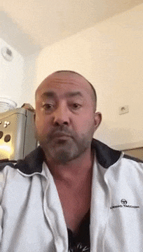 a bald man with a beard is wearing a white jacket .