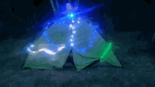 a tent is lit up with blue and green lights and looks like a christmas tree .
