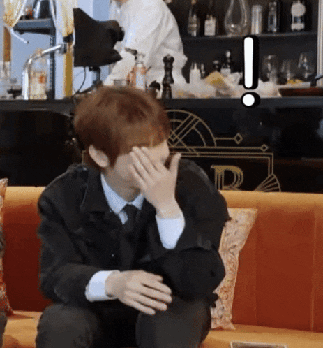 a man sitting on a couch covering his face with his hand