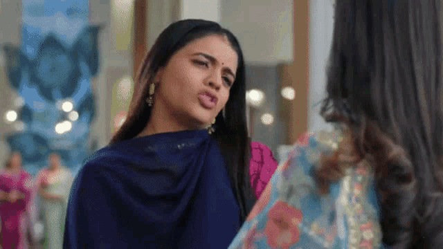 a woman in a blue saree is making a funny face while standing next to another woman in a pink dress .