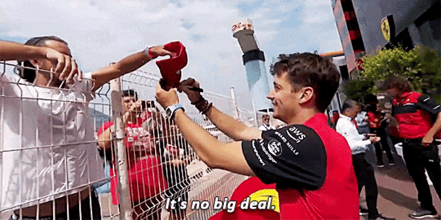 a man in a red shirt says it 's no big deal as he signs a hat for a fan