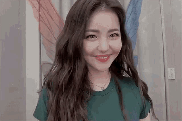 a woman with long hair is wearing a green t-shirt and red lipstick and smiling .