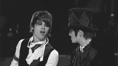 two men are standing next to each other in a black and white photo . one is wearing a top hat .