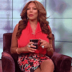 a woman in a red top is sitting in a chair holding a cup of coffee ..