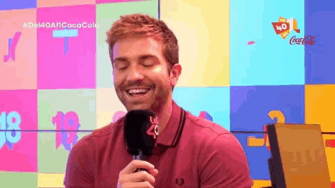 a man in a red shirt is smiling while holding a microphone in front of a coca cola logo