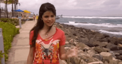 a woman in a red shirt is standing on a sidewalk near the ocean