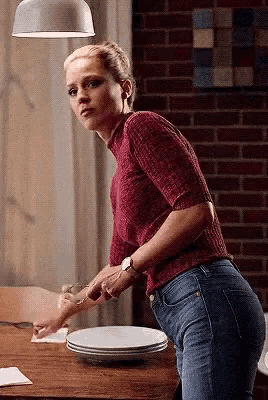 a woman in a red sweater and blue jeans is standing next to a table with plates on it .
