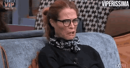 a woman wearing glasses and a scarf is sitting on a couch making a face .