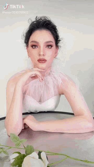 a woman in a white dress is sitting at a table with her hands on her chin and a tiktok watermark on the bottom