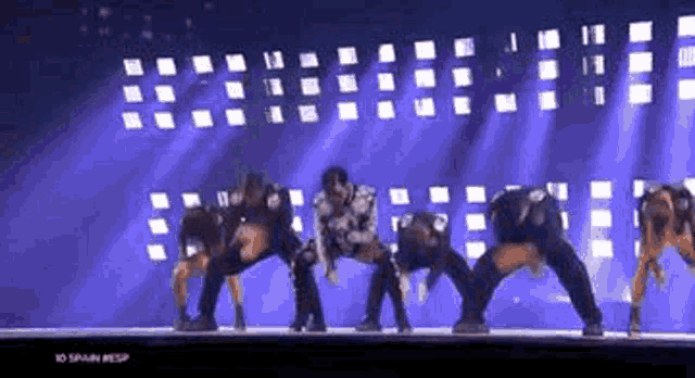a group of dancers are dancing on a stage in front of a blue background .