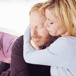 a woman is hugging a bearded man on a couch