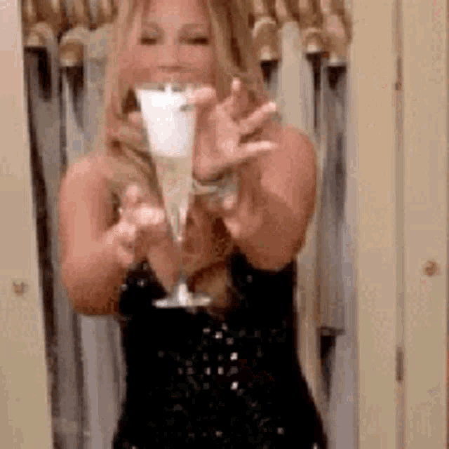 a woman in a black dress is holding a glass of champagne in front of her face .