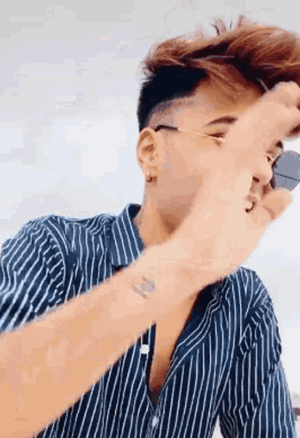 a young man wearing sunglasses and a striped shirt is pointing at his face .