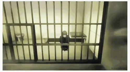 a person is sitting in a jail cell behind bars .