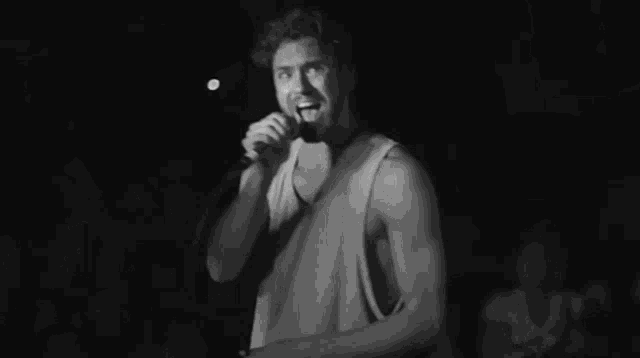 a man in a tank top is singing into a microphone in front of a crowd .
