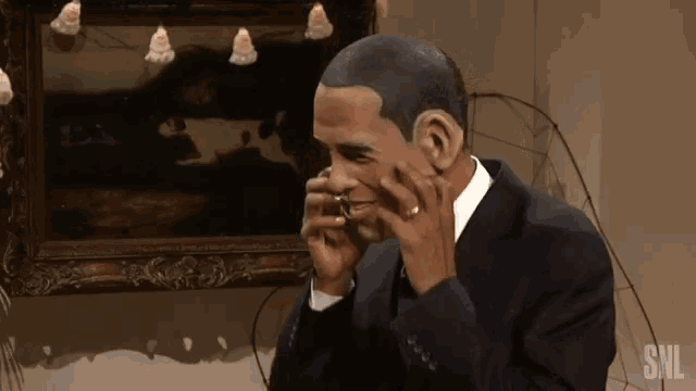 a man in a suit talking on a cell phone with snl written on the bottom right