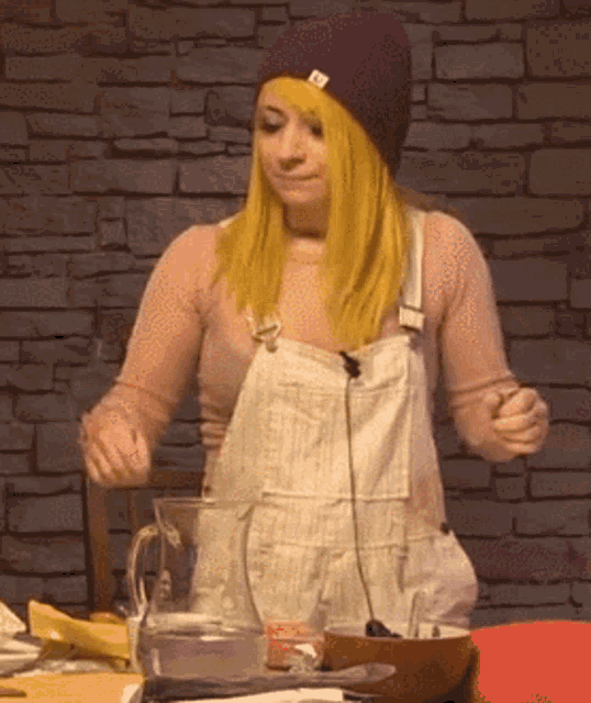 a woman with yellow hair is wearing overalls and a purple beanie ..