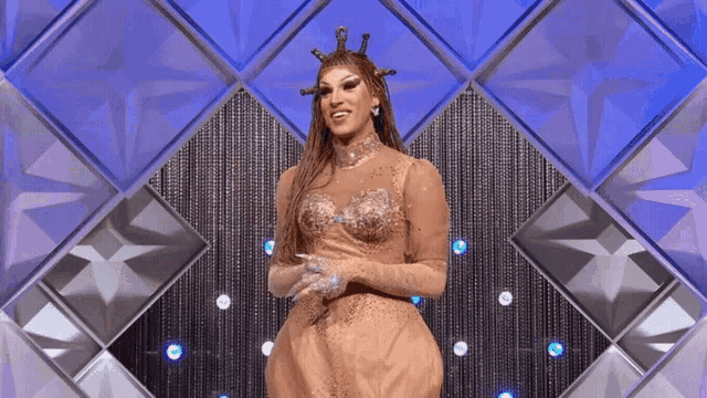 a woman in a dress with a crown on her head stands in front of a diamond backdrop