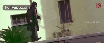 a man in a hooded jacket is walking down a sidewalk next to a building .