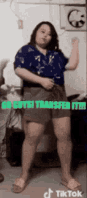 a woman in a blue shirt and shorts is dancing in front of a mirror with the words `` go guys transfer it ! ''