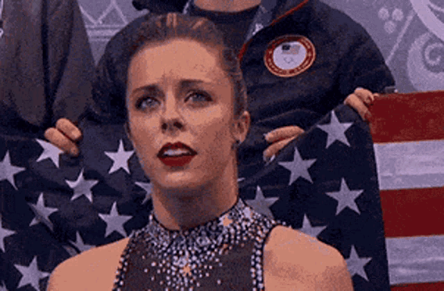a female figure skater is standing in front of an american flag .