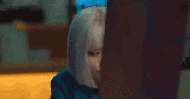 a woman with blonde hair is peeking out from behind a wall and making a funny face .