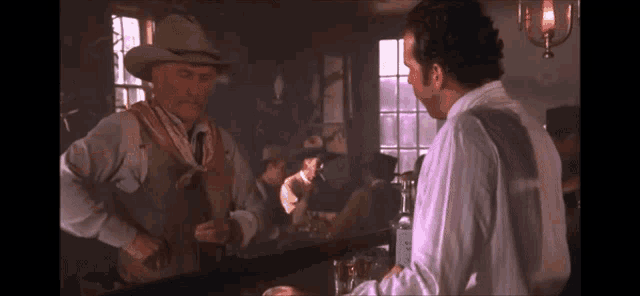 a man in a cowboy hat is talking to a man in a white shirt