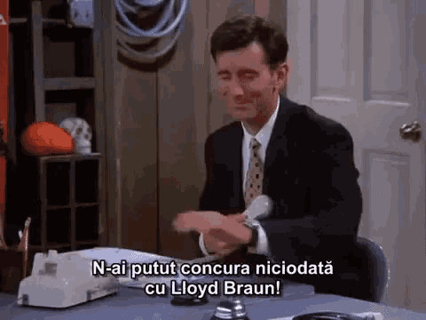 a man in a suit and tie is sitting at a desk in front of a telephone and talking to lloyd braun .