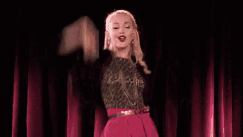a woman in a leopard print top and a pink skirt is standing in front of a red curtain .
