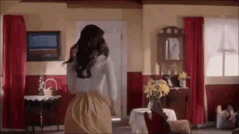 a woman is standing in a living room with a vase of yellow flowers on a table .