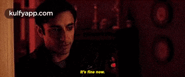 a man is standing in a dark room with a red light behind him and says `` it 's fine now '' .